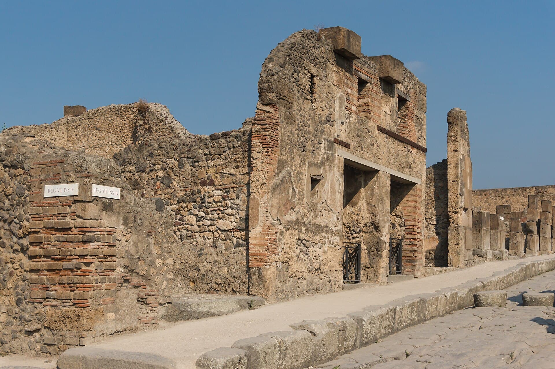 A two-story house front on a Pompeii street, with a brick doorway and a stone sidewalk.